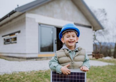 Portrait of little boy holding solar panel, in front of their new unfinished house.