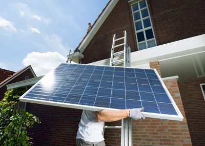 Worker climbing ladder carrying solar panel for roof of new home, California