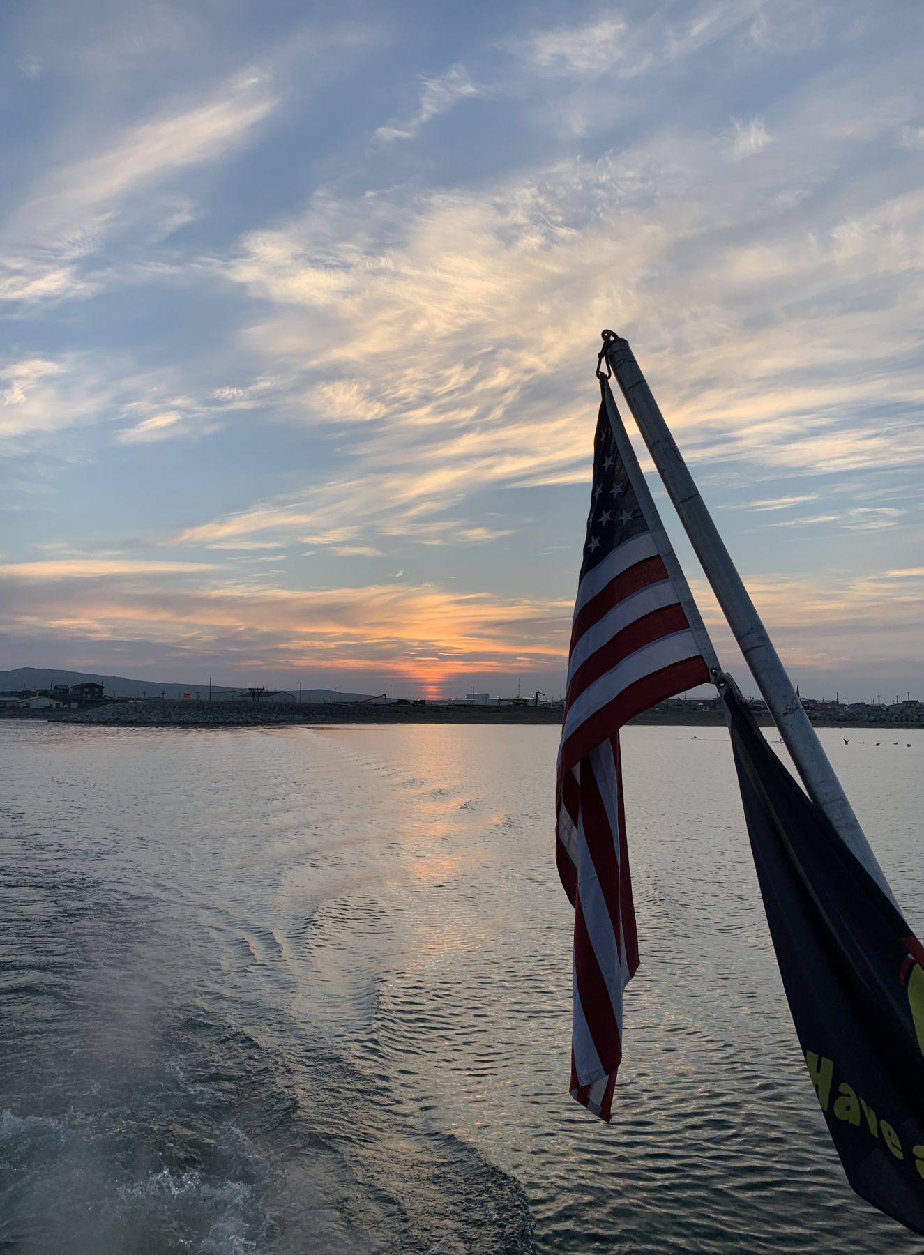 An American flag flying from the stern of a boat at sunset on the water